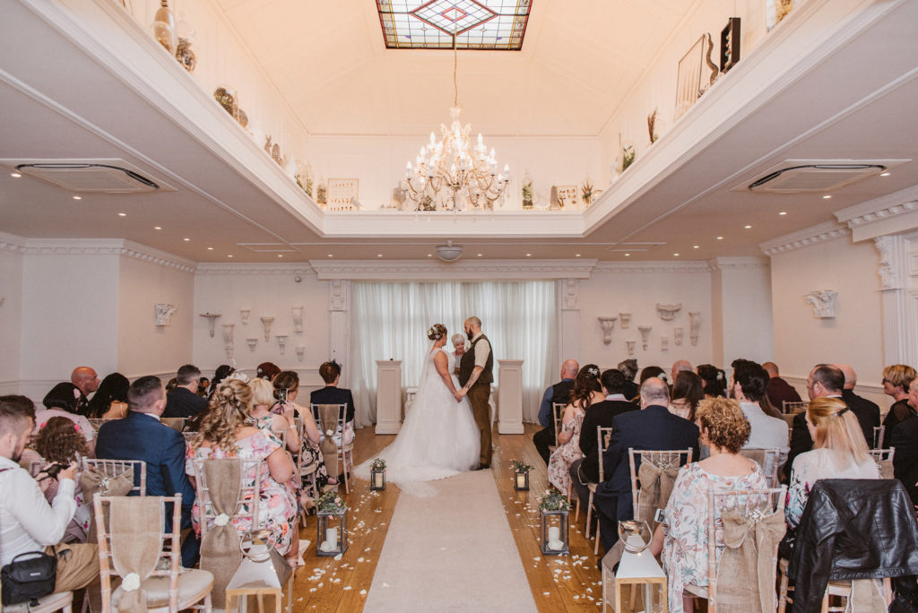 Wide angle view of the bride and groom holding hands at the end of the aisle during the wedding ceremony at Ashfield House