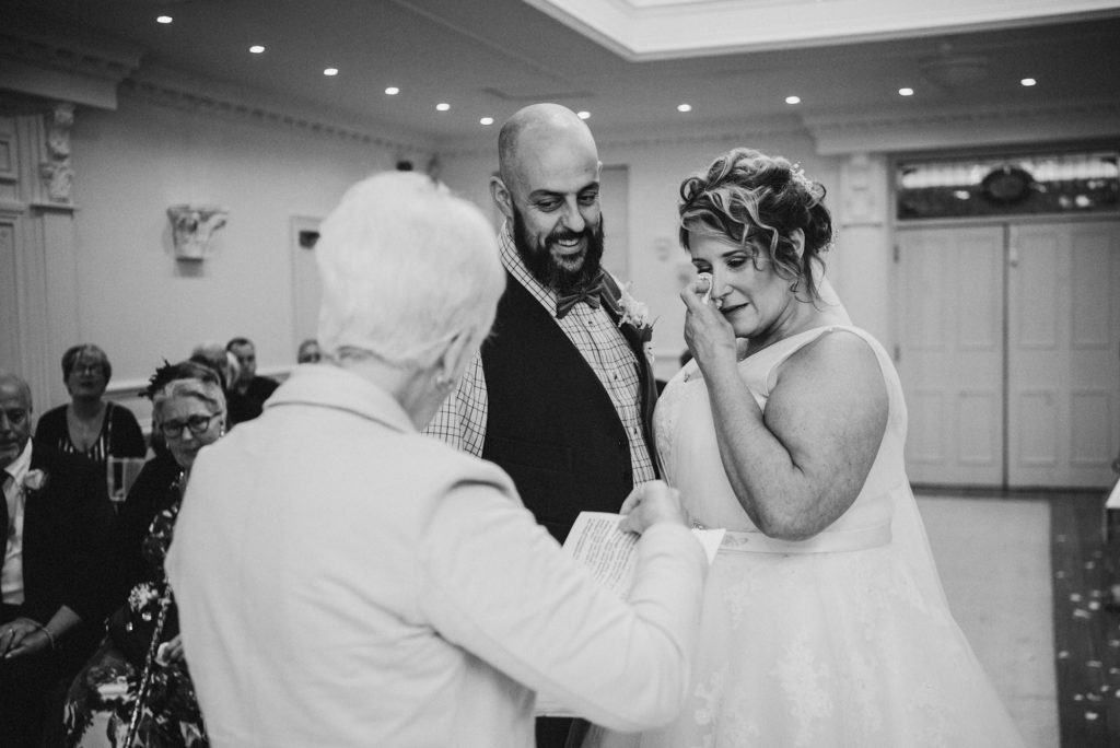 Bride wipes her eye with a tissue during the wedding ceremony at Ashfield House