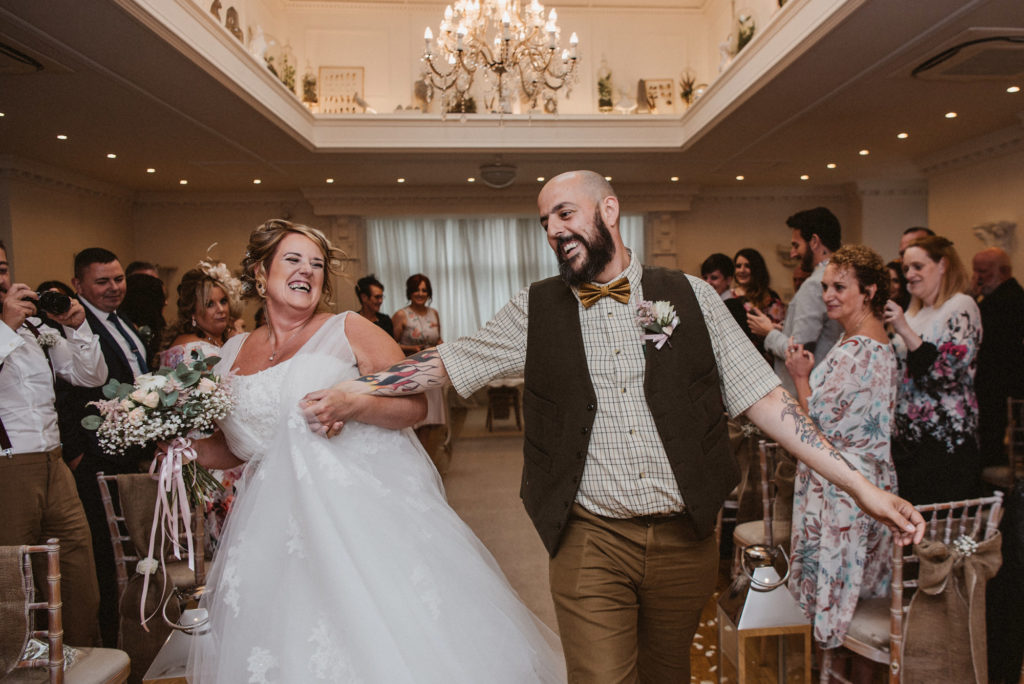 Bride and groom skip merrily down the aisle in the langtree suite at Ashfield House