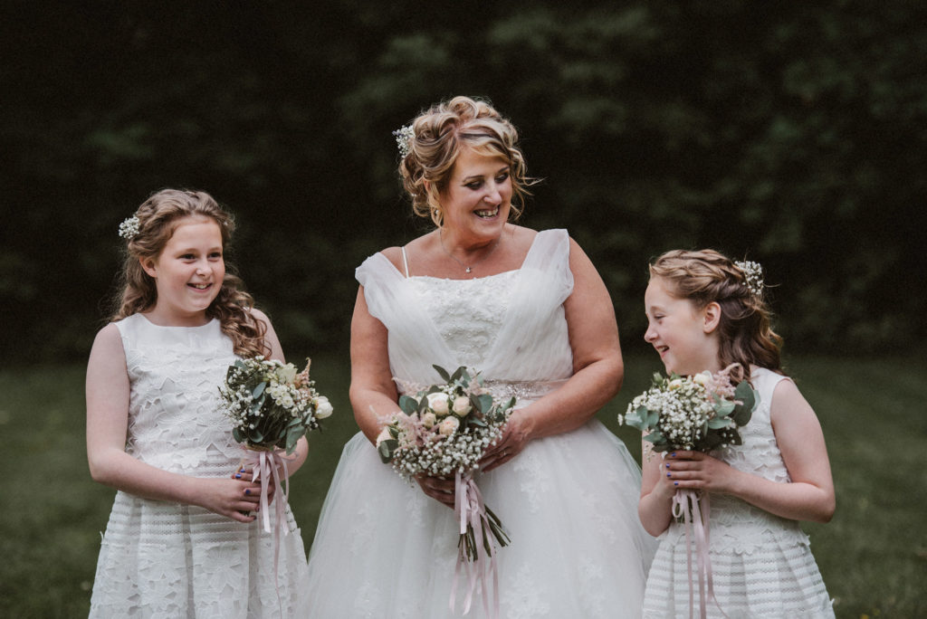 Bride laughs with her two young bridesmaids in the gardens at Ashfield House