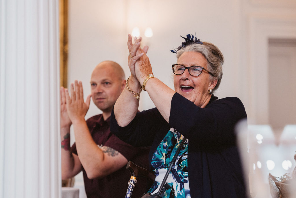 The mother of the groom claps excitedly in response to a joke told by the groom during the wedding speeches
