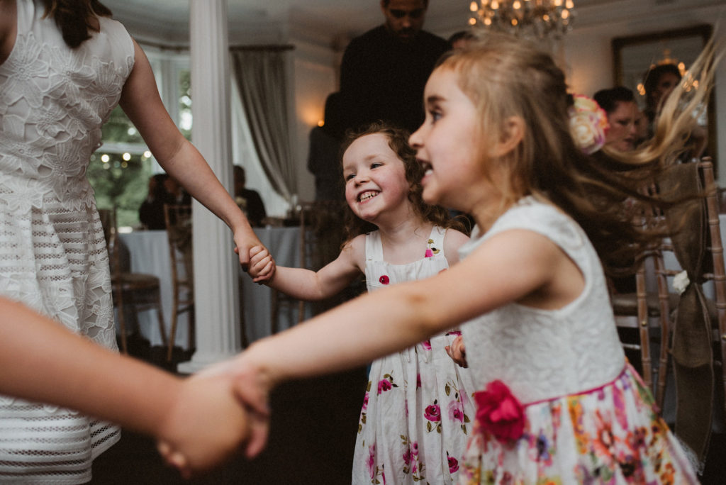 Three girls hold hands and dance in a circle during a wedding reception
