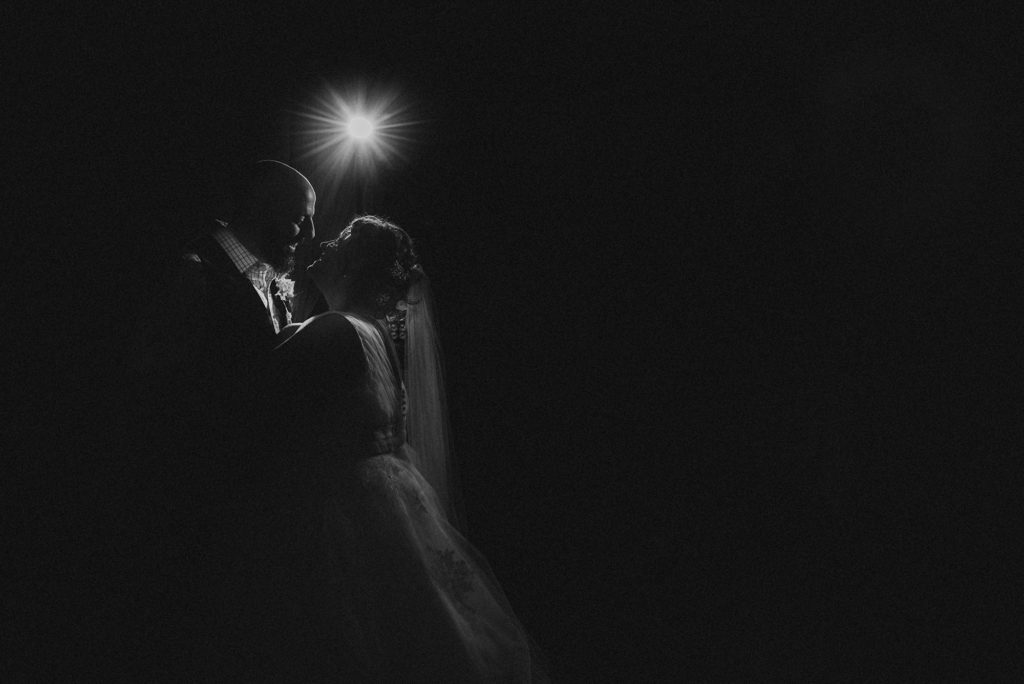 The bride and groom look into each other's eyes during the first dance in front of a dramatic bright light