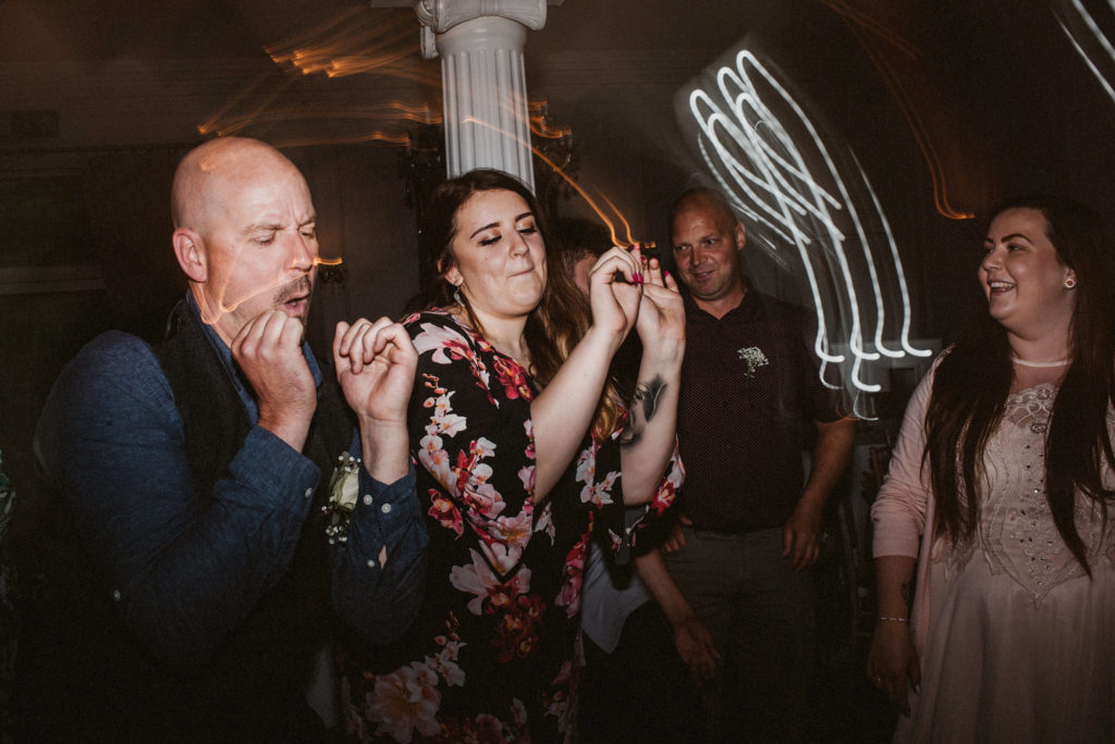 Two wedding guests make silly faces whilst dancing in synch with each other at a wedding reception