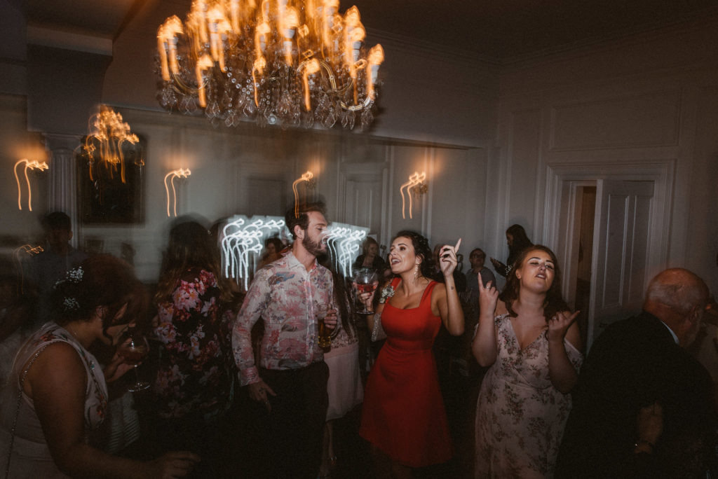 Three wedding guests dance excitedly to loud music at a wedding reception