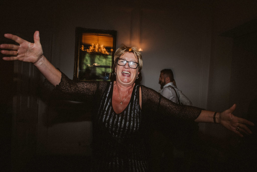 A woman looks straight into the camera with her arms outstretched during a wedding reception