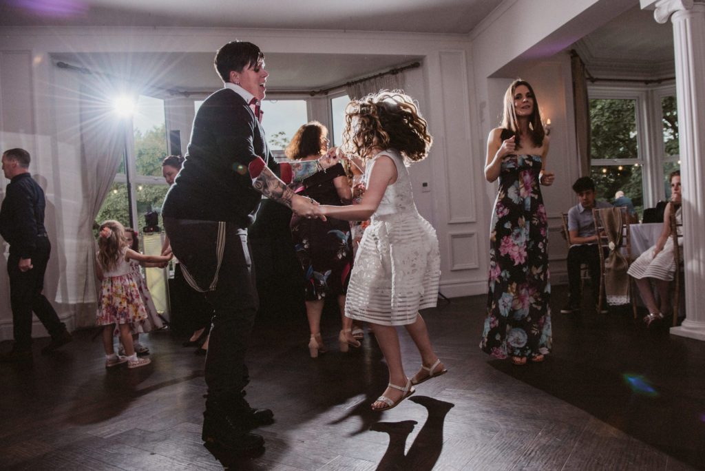 A girl in a white dress jumps up and down on the dance floor at a wedding