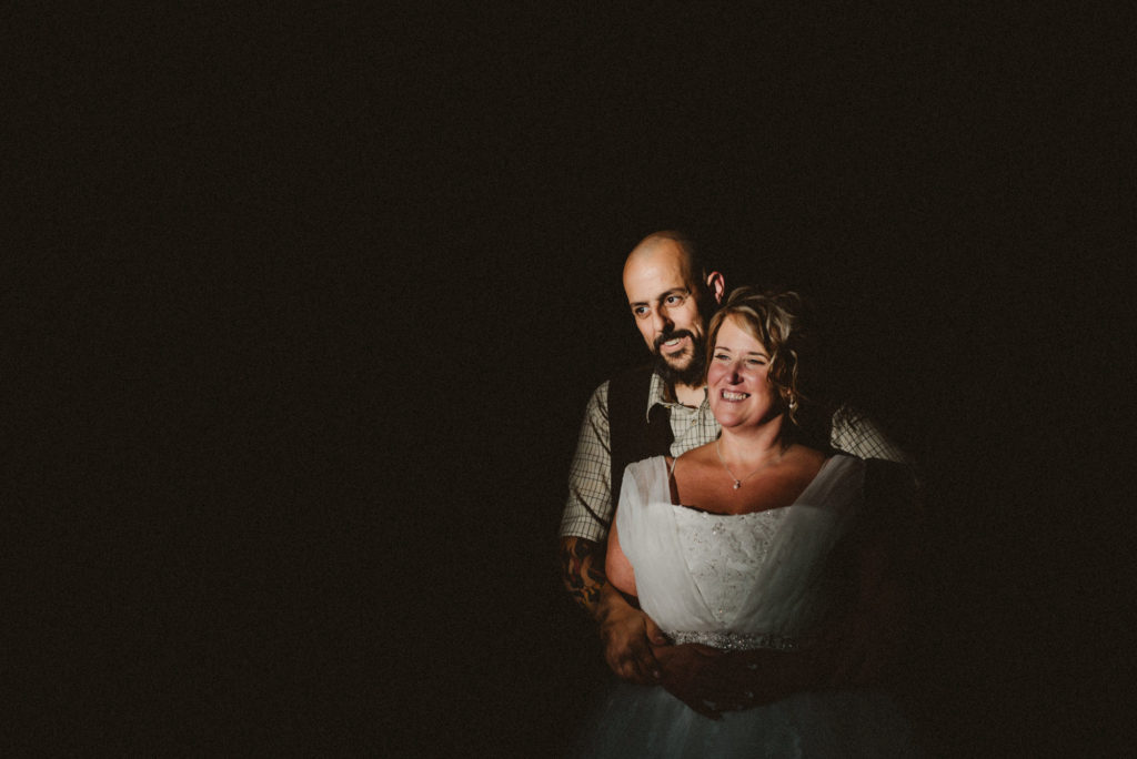 A bride and groom look into the distance whilst holding each other in a patch of light at golden hour