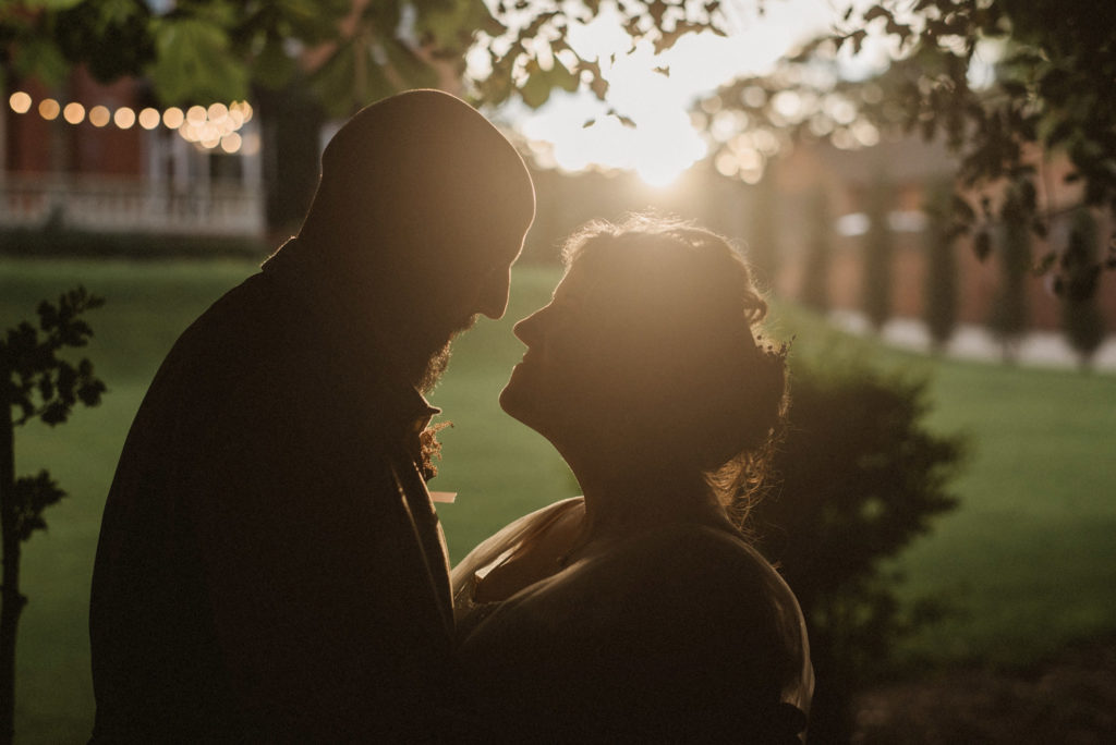 Bride and groom stand and look at each other during golden hour with their faces silhouetted