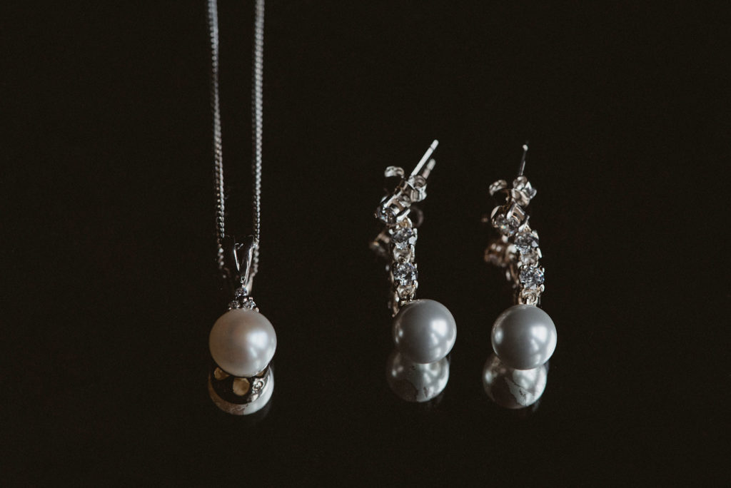 Pearl and silver necklace and pearl and diamond earrings sitting on reflective surface