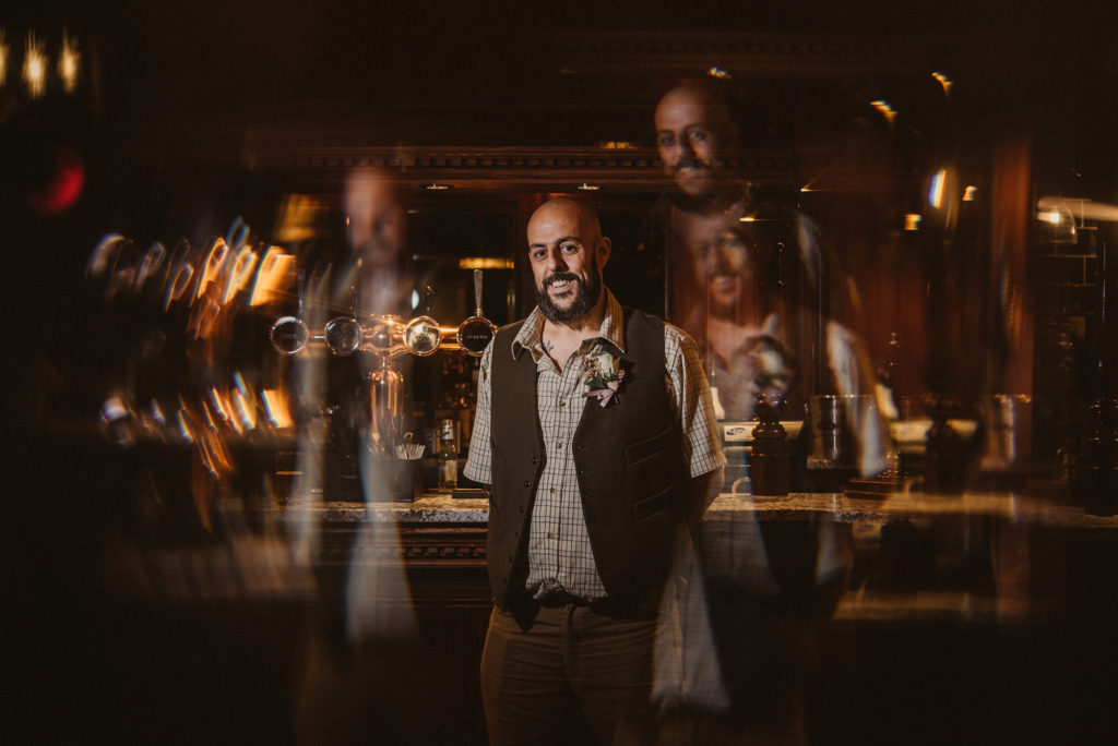 Groom looks directly at camera reflected through a stained glass door