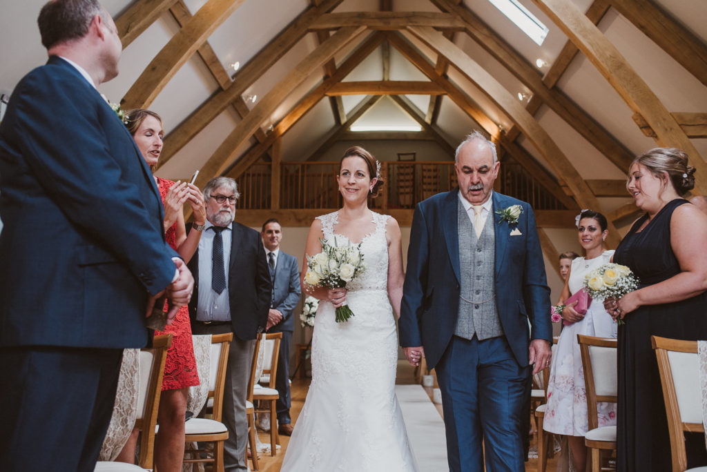 bride and her father walk up the aisle in the Ceremony Barn at Easton Grange