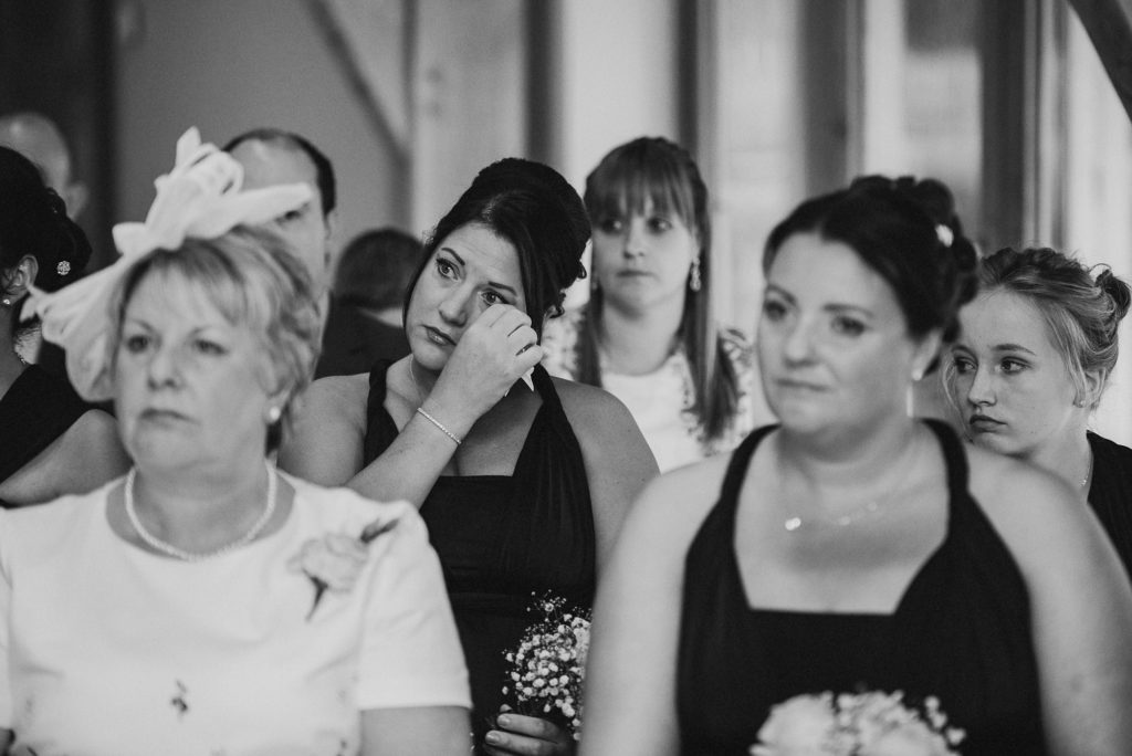 bridesmaid emotionally wipes her eye during her friend's wedding ceremony