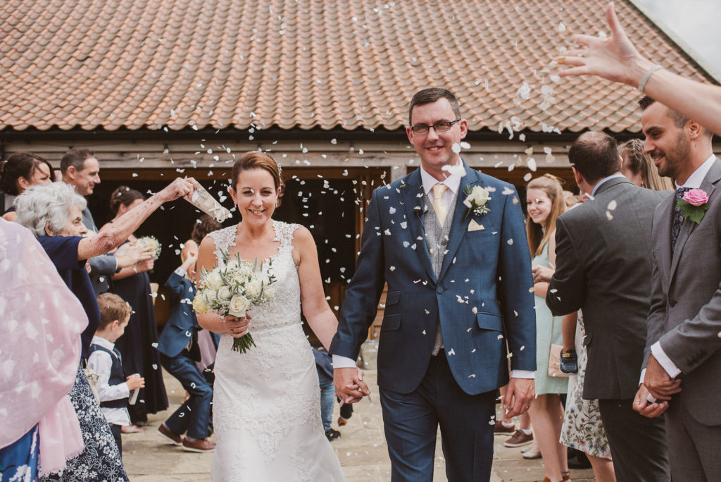 bride and groom get confetti thrown at them at their Surrey barn wedding
