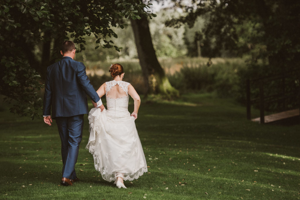 groom holds the back of bride's dress as she walks along
