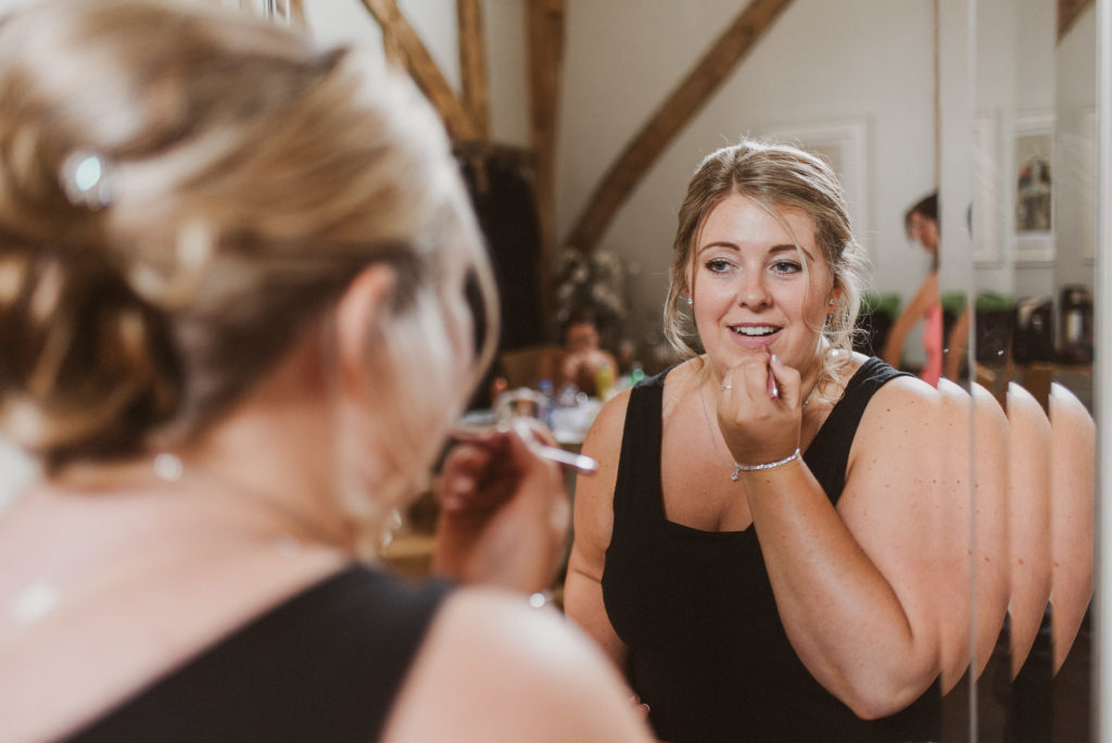 bridesmaid looking into a mirror and putting lipstick on at Easton Grange