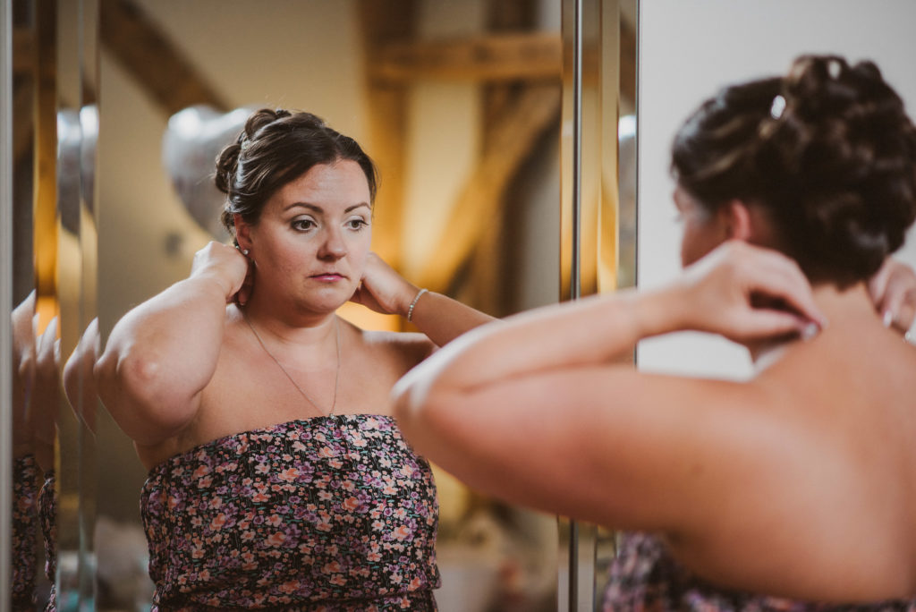 bridesmaid putting a necklace on and looking into the mirror at Easton Grange