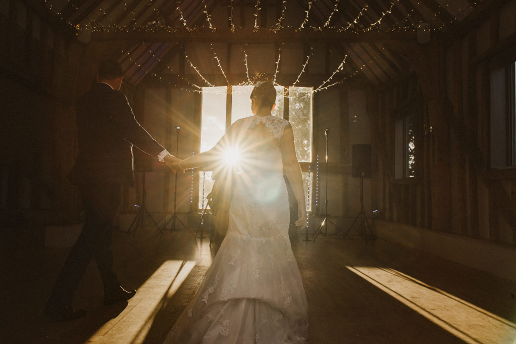 bride and groom walk towards their first dance in the sunlight at golden hour
