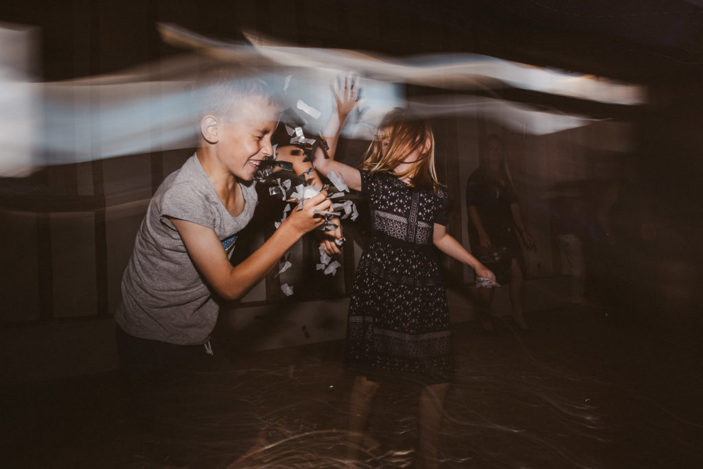 children throw confetti at each other at a barn wedding reception