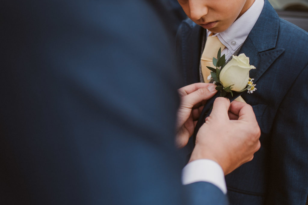 groom places buttonhole flower on his sun at Easton Grange