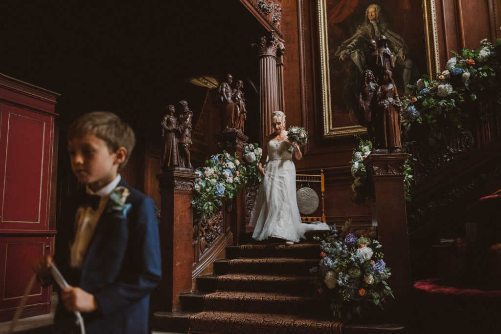 bride walks down beautiful grand staircase to meet her groom during her wedding ceremony in the Great Hall at Cliveden House