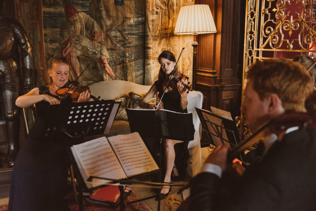 a musician plays the violin during a wedding ceremony in the Great Hall at Cliveden House