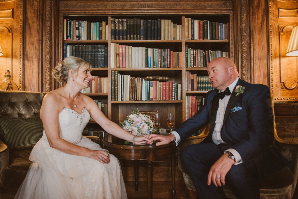 bride and groom hold hands and look at each other in front of old books in the library