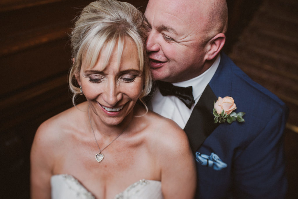 groom whispers something into the ear of his bride which makes her laugh