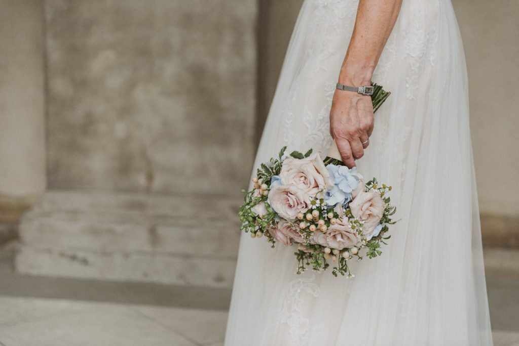 bride holds beautiful bouquet with pink roses next to her wedding dress