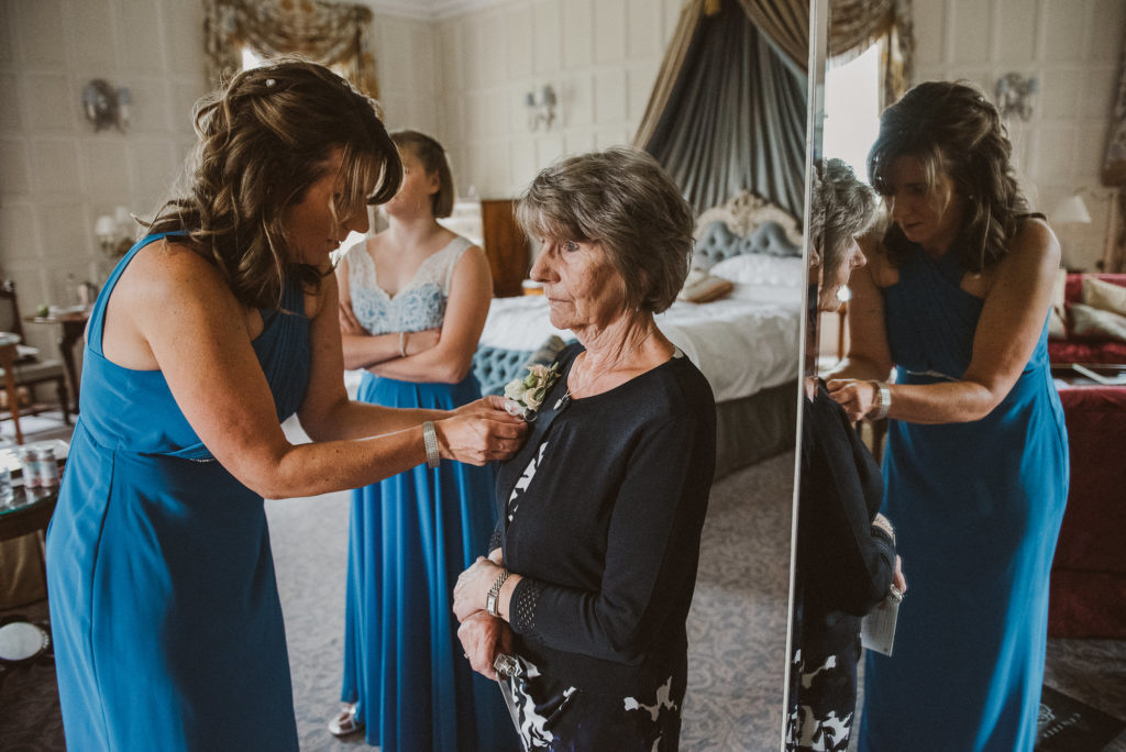 bridesmaid puts buttonhole on mother of the bride in the Lady Astor Suite