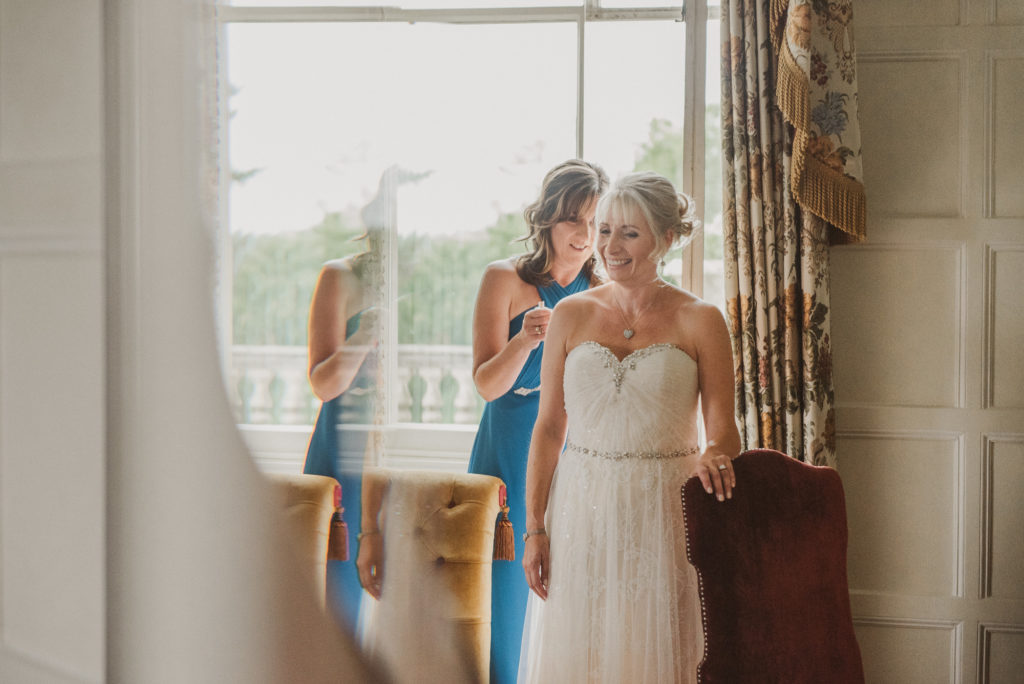 bride gets dress buttoned up in front of window in the Lady Astor Suite