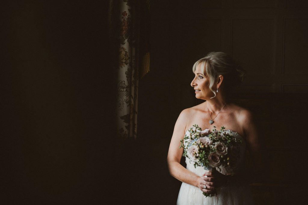 Berkshire bride holds bouquet and looks out window in the Lady Astor Suite prior to her wedding at Cliveden House