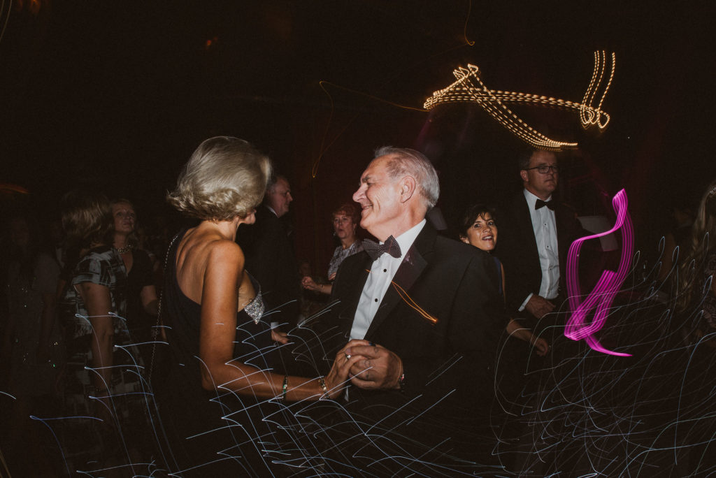a woman in a black dress and a man in black tie dance together during a wedding reception