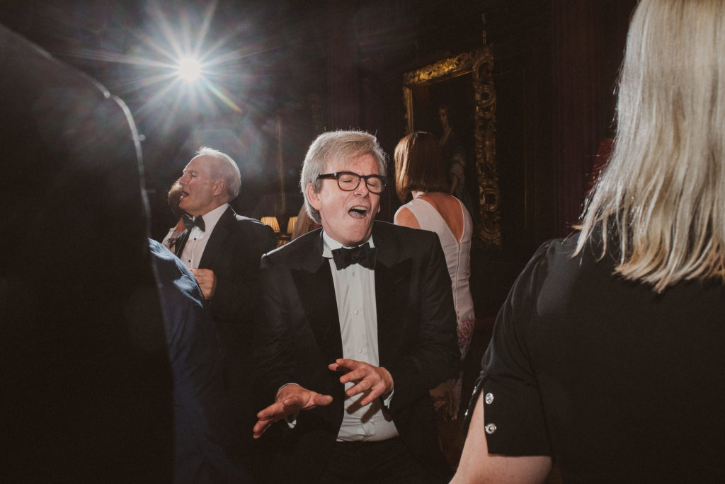 a wedding guest in glasses and a bow tie dances during a wedding reception