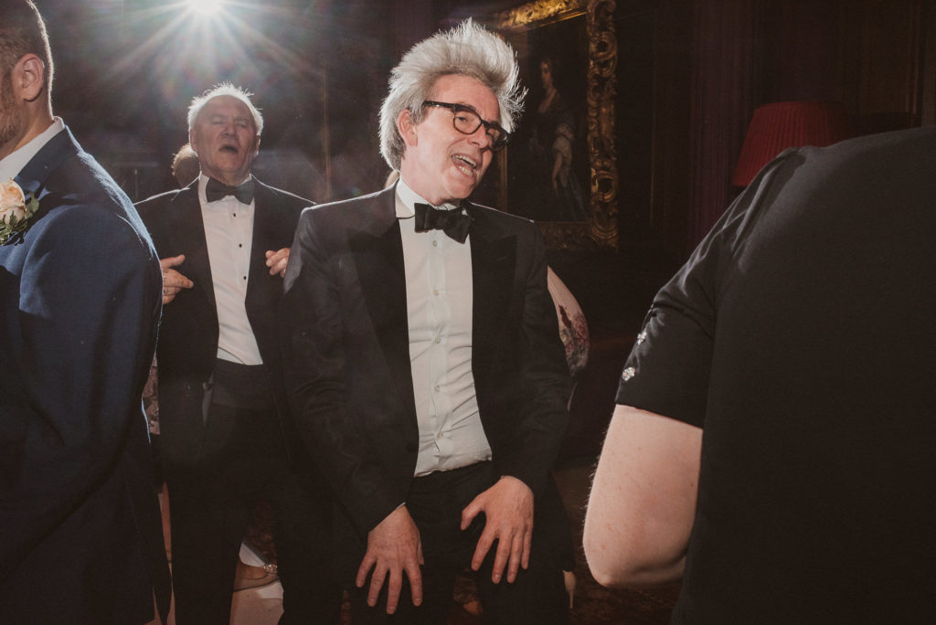 a wedding guest in a bow tie lets his hair down and dances at a wedding in the Great Hall