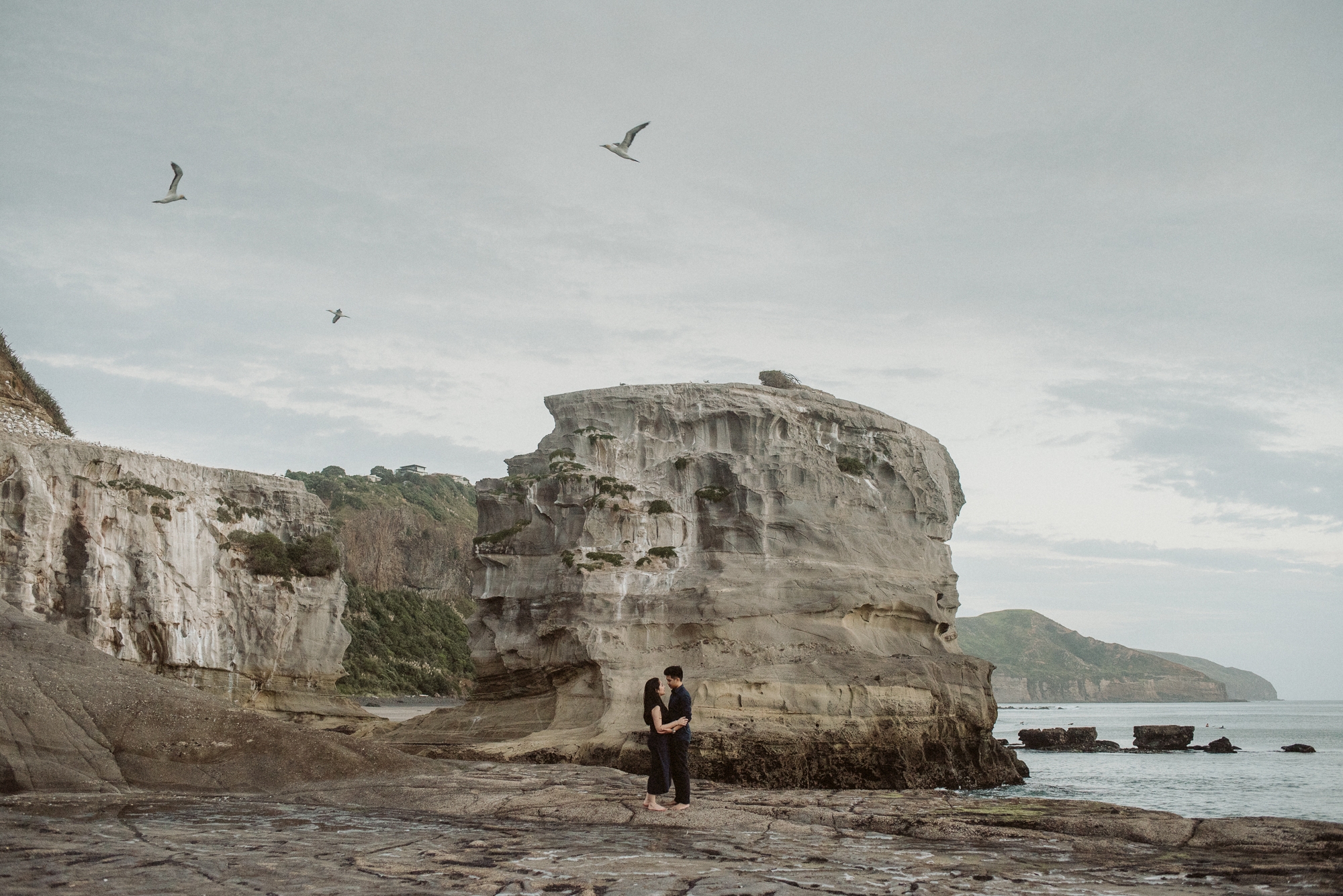 A couple embrace next to the rocks at the gannet colony at Muriwai Beach on the West Coast of Auckland