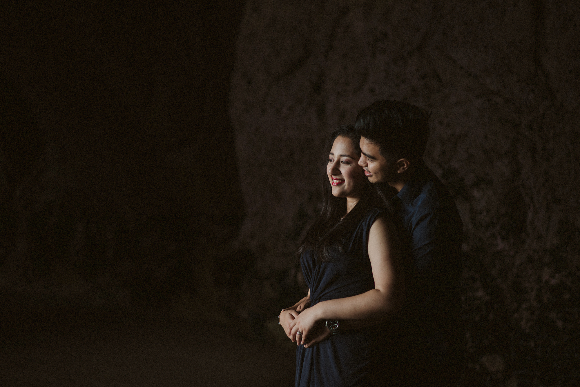 An engaged couple stand in the light in a cave at Maori Bay in Auckland, New Zealand