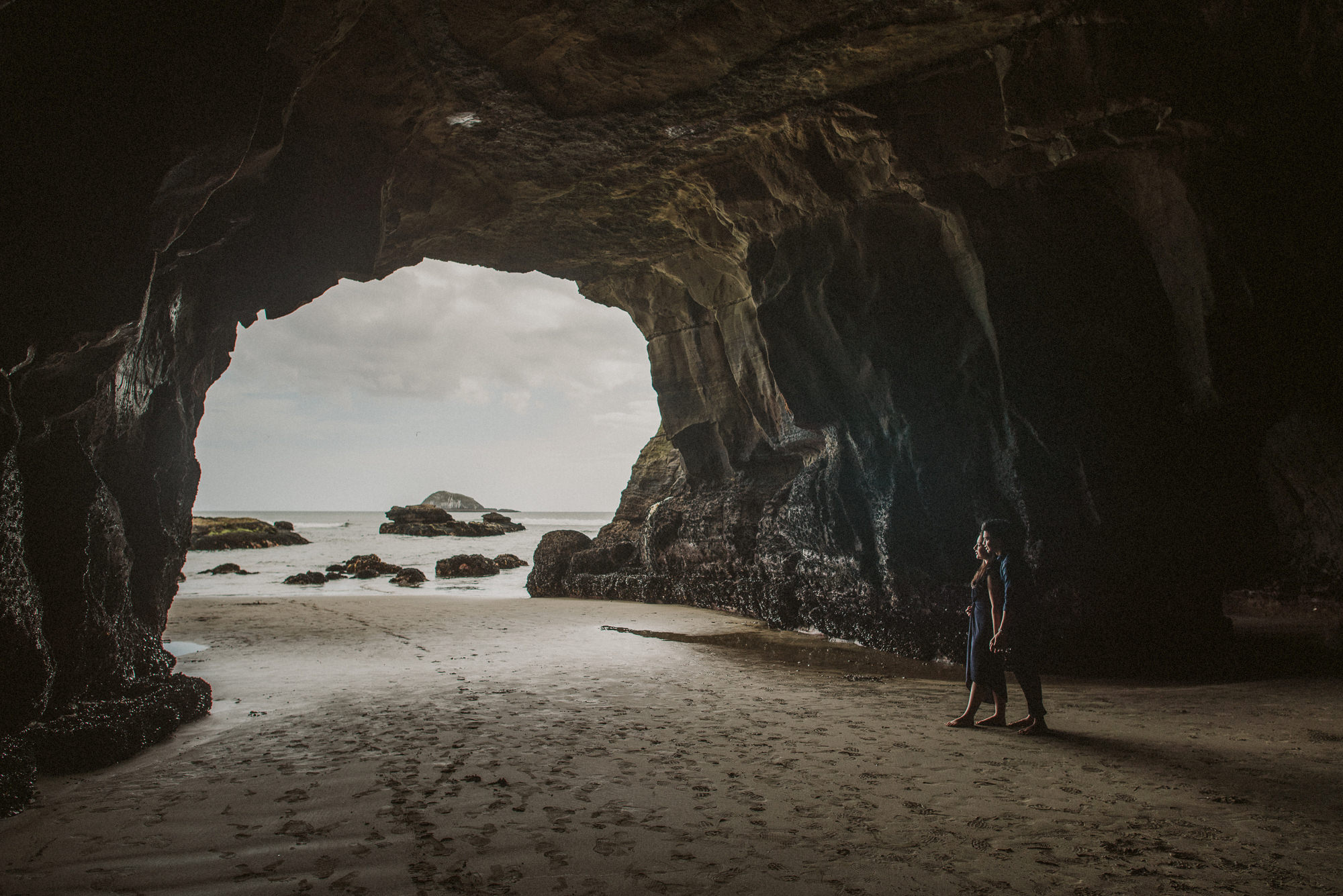 An engaged couple stand inside the cave at Maori Bay on Auckland's West Coast