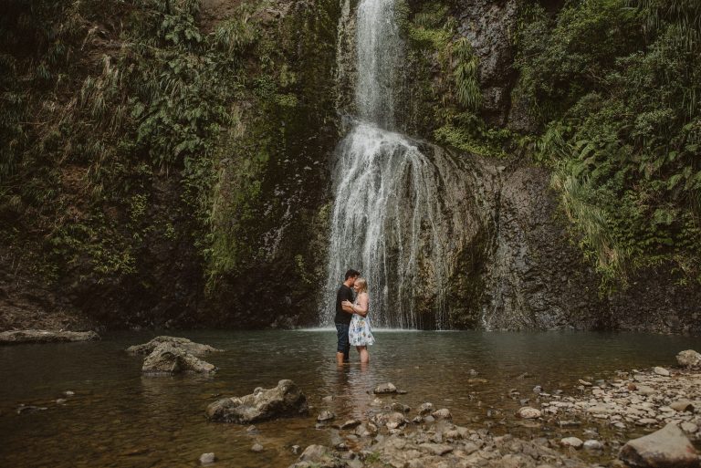 A recently engaged couple hold each other under the waterfall at Kitekite Falls in the Waitakere Ranges