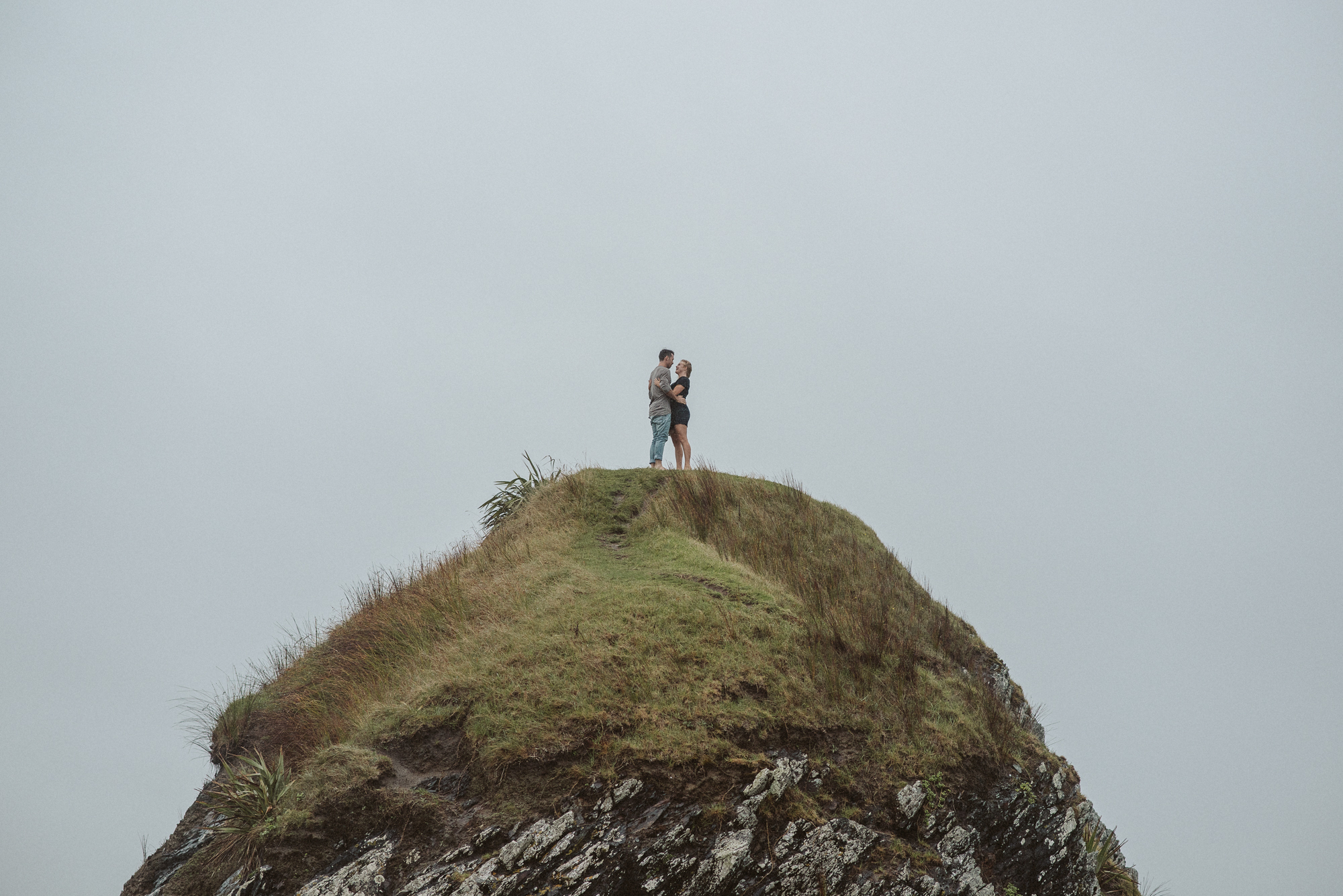 A man and woman on top of a hill having a cuddle in the Tawharanui Regional Park in Auckland