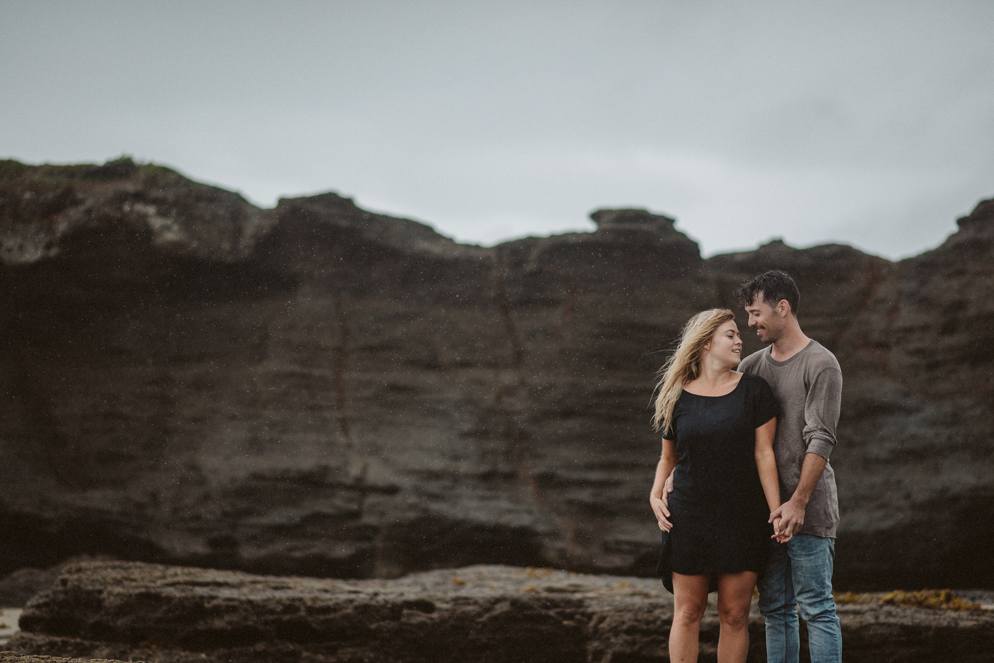 A couple stands next to one another on some rocks on the Tawharanui Peninsula
