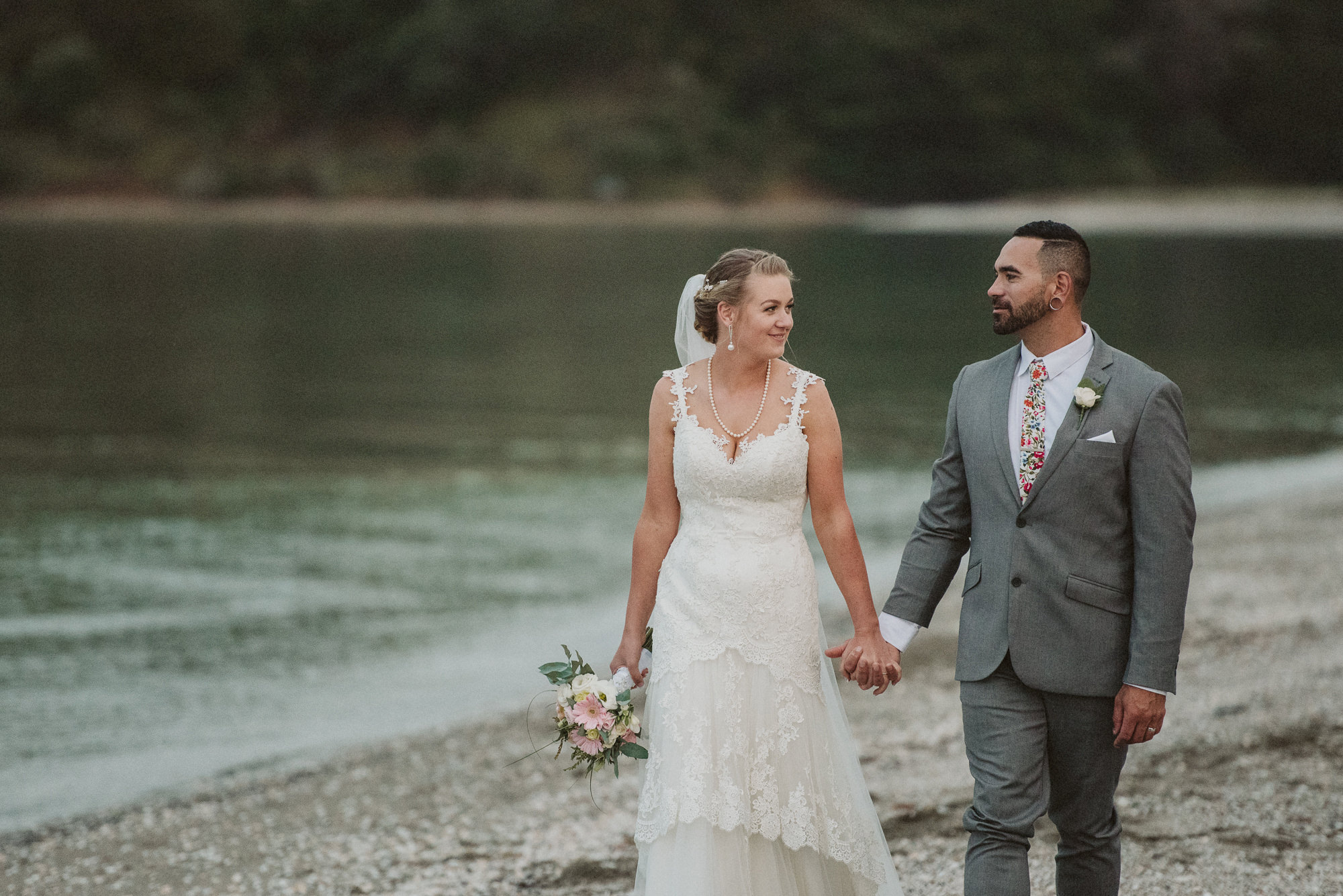 A couple look at each other whilst walking along Maraetai Beach hand in hand