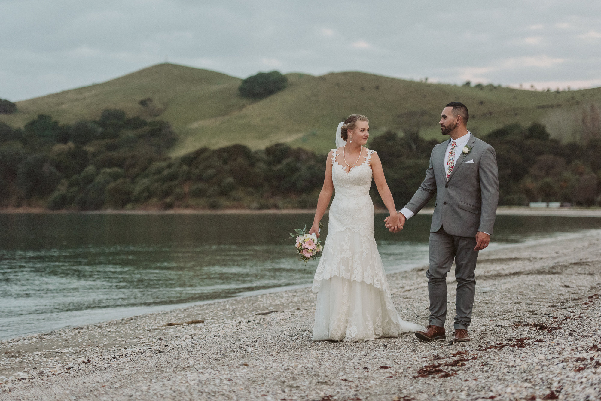 A happy couple hold hands and walk along Maraetai Beach next to the sea