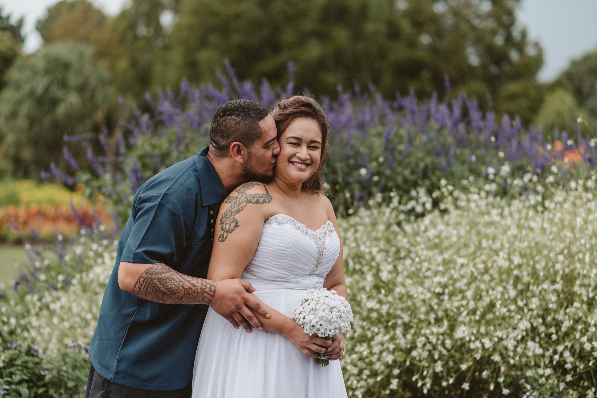 A couple laugh and kiss in front of some flowers at Auckland Botanic Gardens